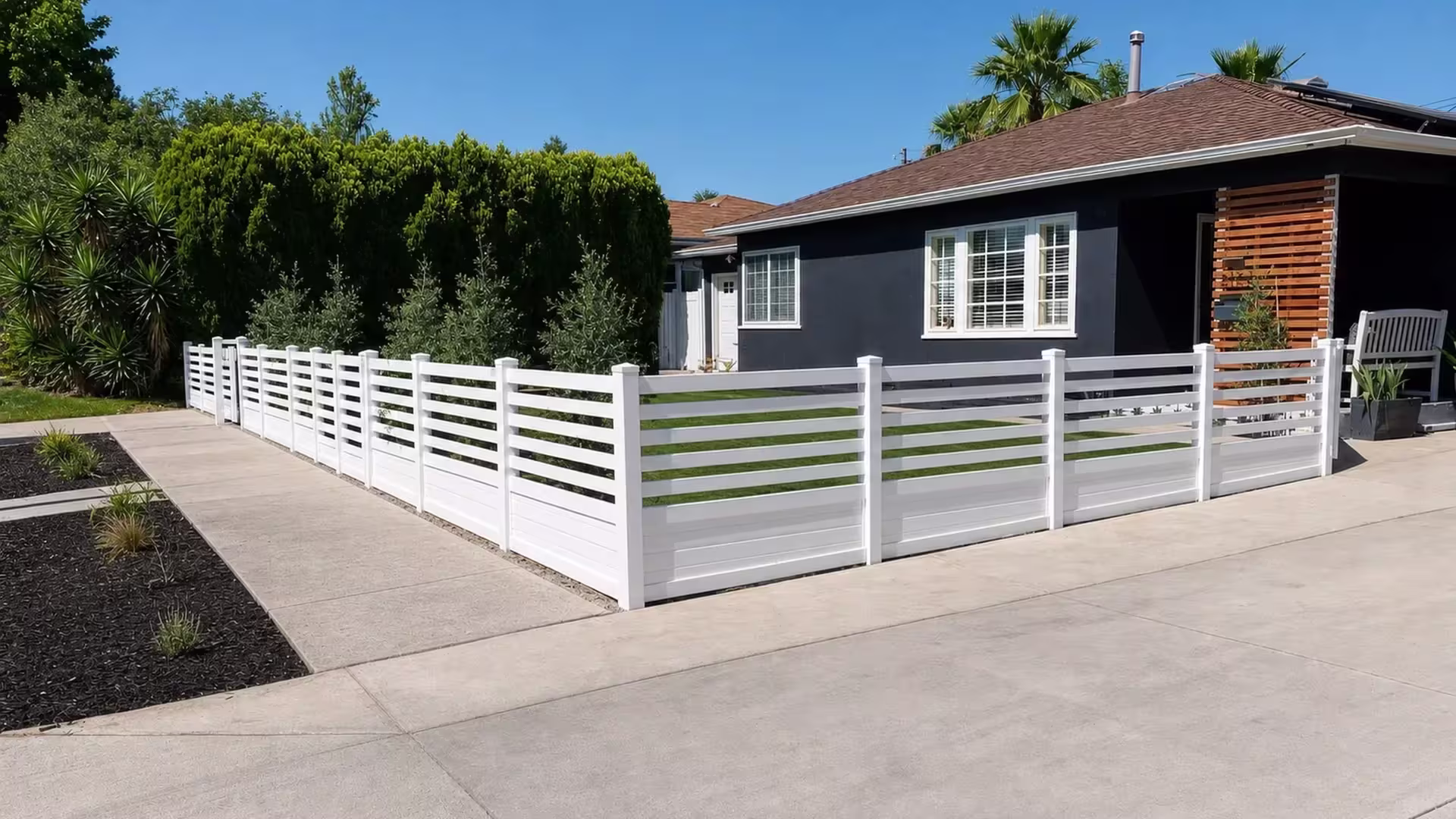 A White vinyl picket fence turns a right angle beside an existing wood privacy screen near the entry
