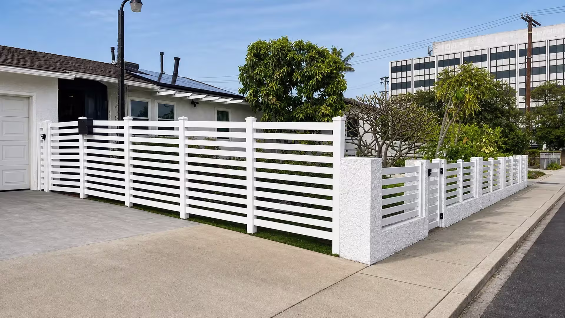 Tall White vinyl picket fence meets a stucco corner wall beside a black mailbox post