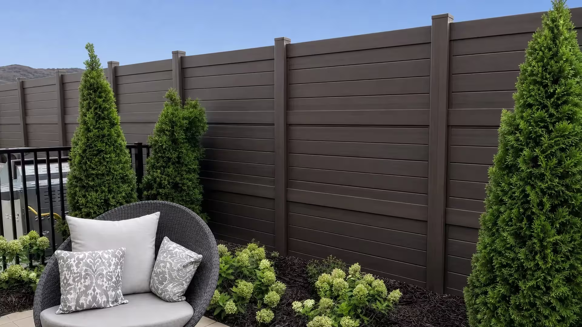 Dark Walnut vinyl horizontal privacy fence running past a hydrangea bed and a woven patio chair