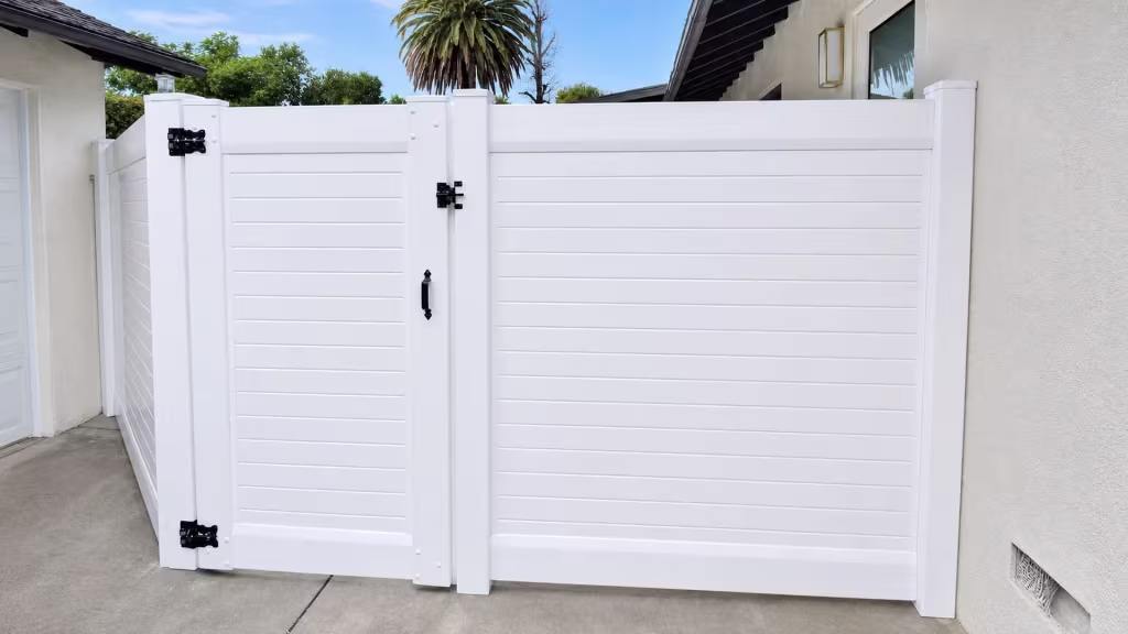 Two stucco buildings frame a White vinyl horizontal privacy fence filling the passage between them