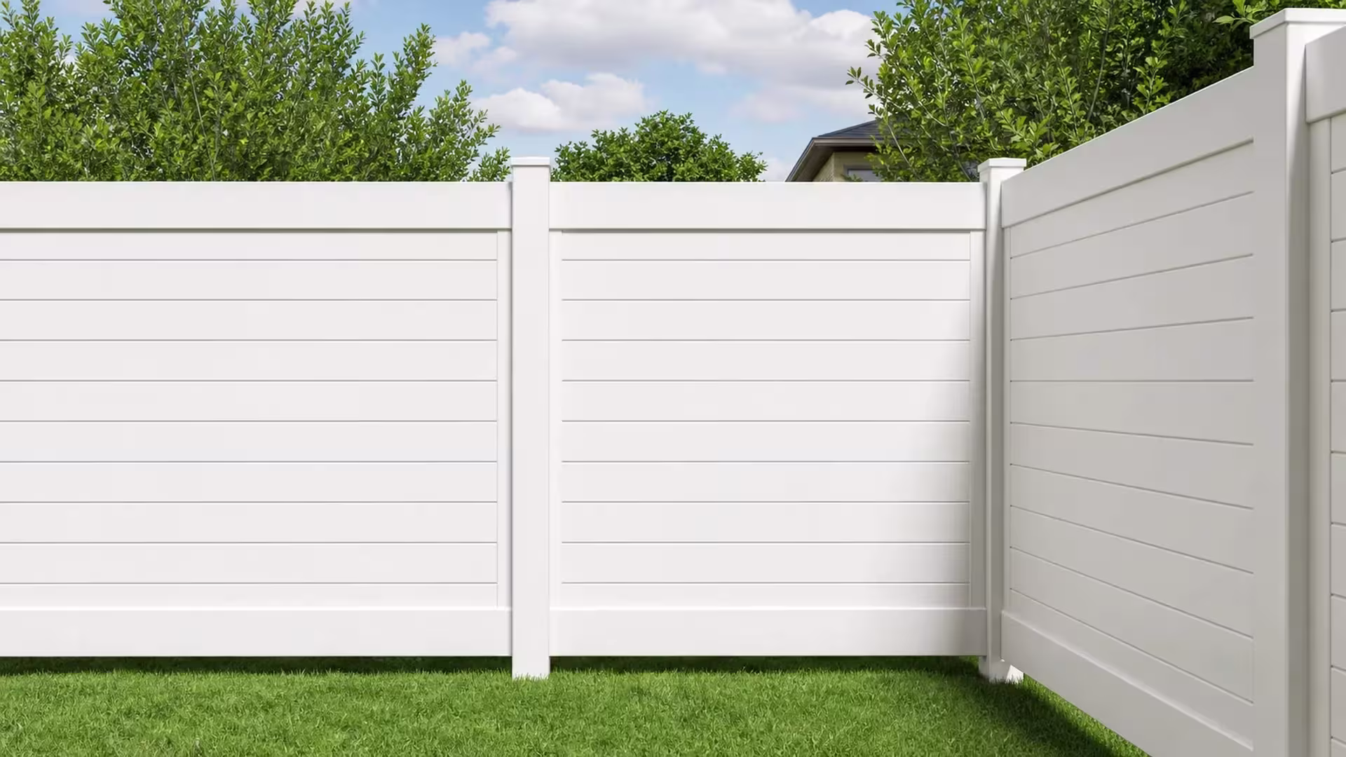 An open green lawn is cornered by a White vinyl horizontal privacy fence under a cloudy sky