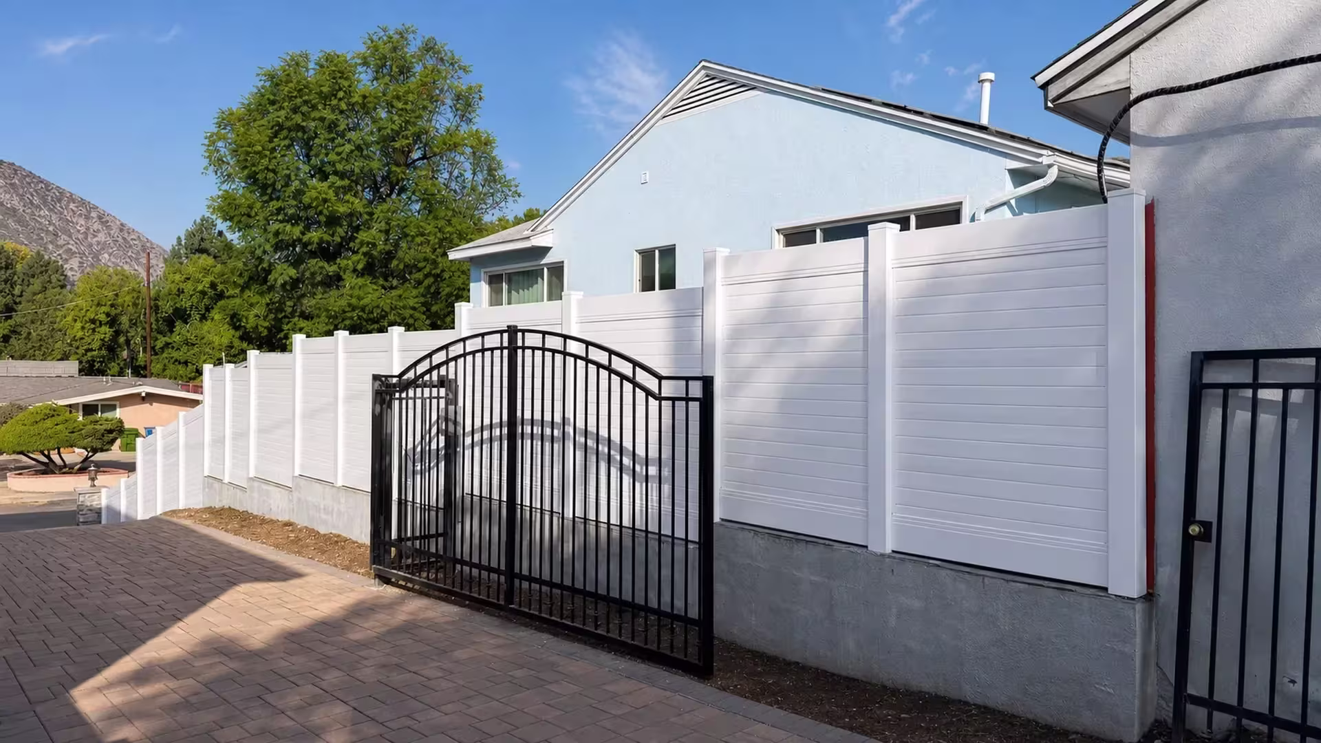 A sloped property falls away beneath a White vinyl horizontal privacy fence mounted on a concrete retaining wall