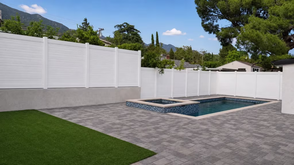 A stucco masonry wall raises a White vinyl horizontal privacy fence over a pool and spa