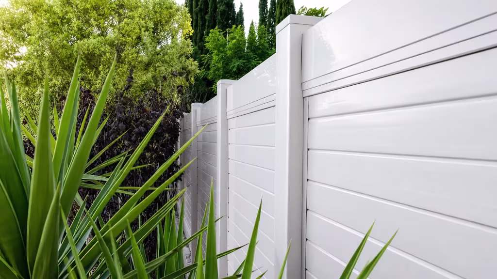 Burgundy hedge and cypress trees surround a White vinyl horizontal privacy fence through dense landscaping