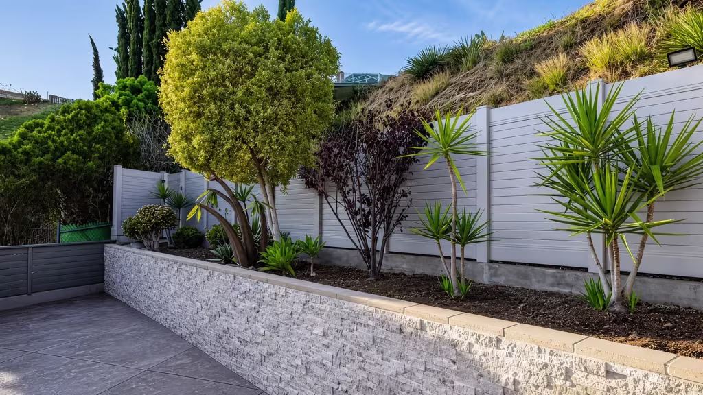 A raised planting bed fronts a White vinyl horizontal privacy fence above a textured retaining wall