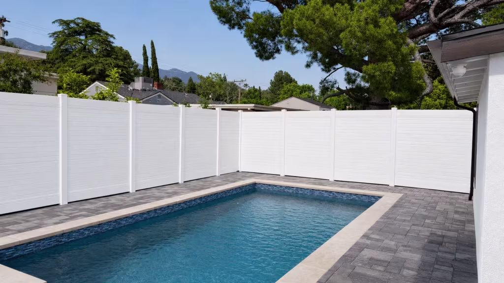 An L-shaped pool yard is bordered by a White vinyl horizontal privacy fence beside a stucco house
