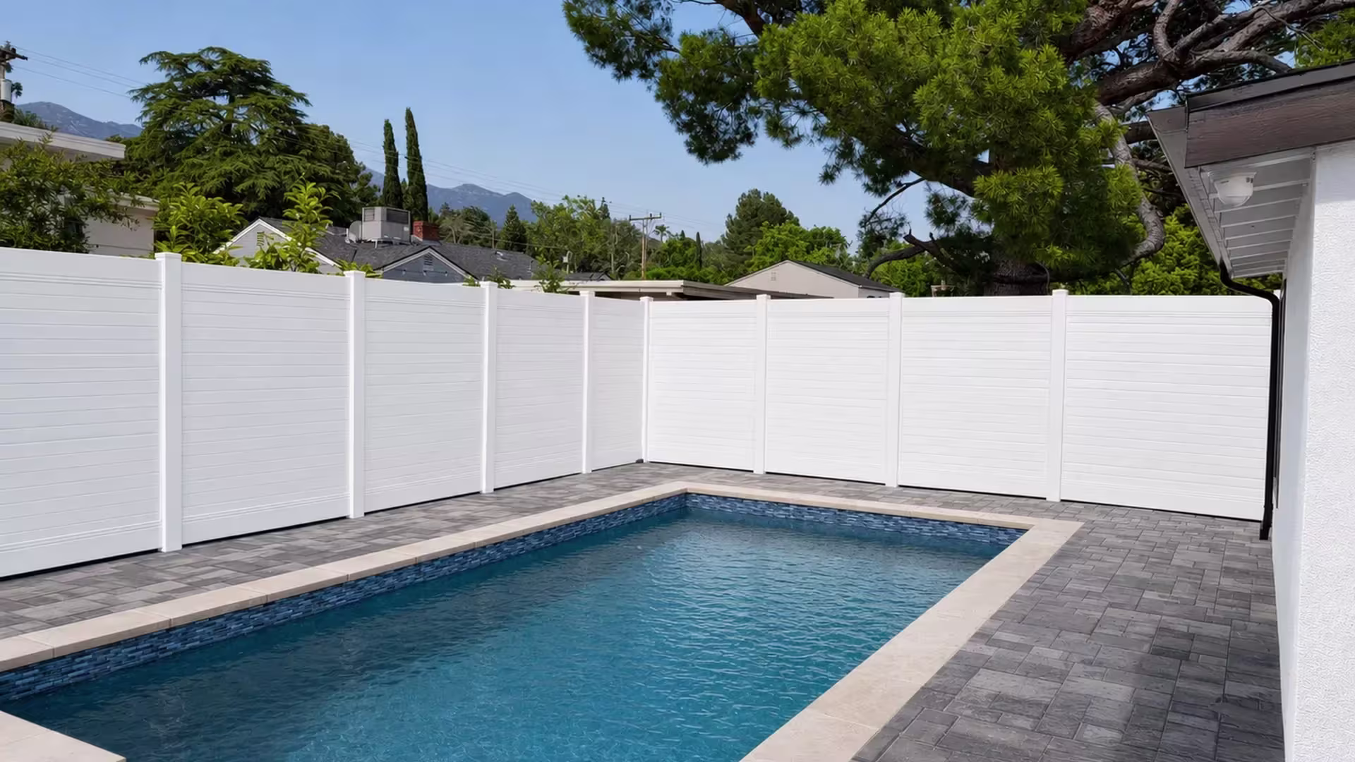 An L-shaped pool yard is bordered by a White vinyl horizontal privacy fence beside a stucco house