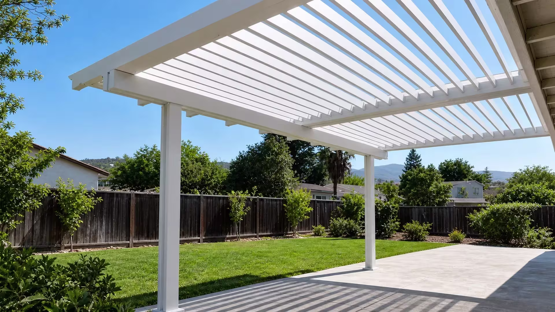 A ridge of distant hills rises past the fence line behind this White vinyl picket patio cover