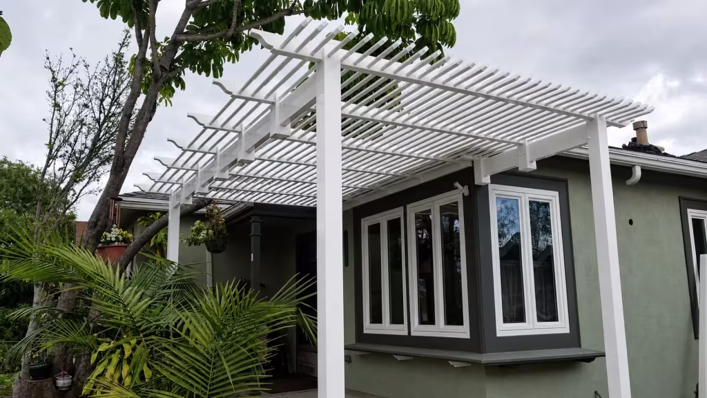 A sage green house wall and chimney vent surround this White vinyl picket patio cover