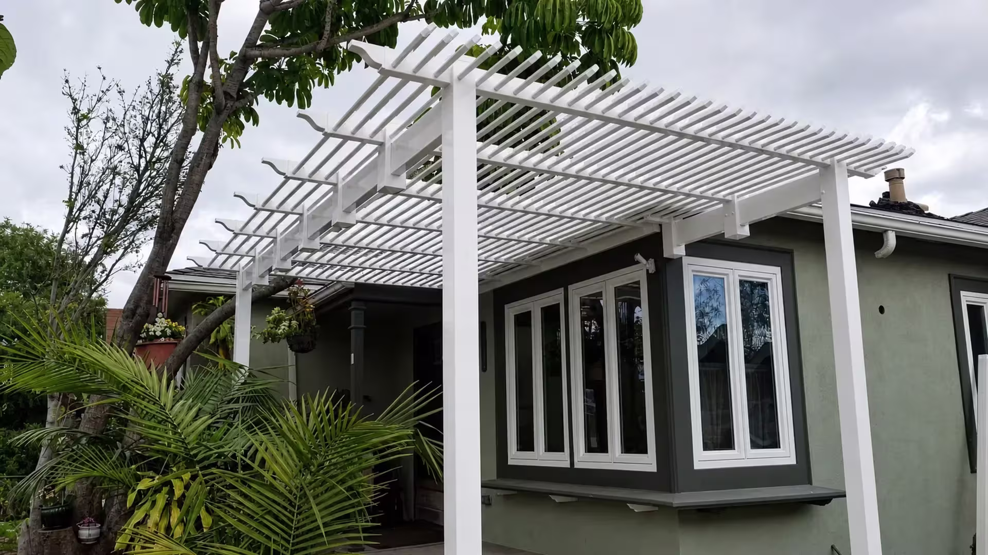 A sage green house wall and chimney vent surround this White vinyl picket patio cover