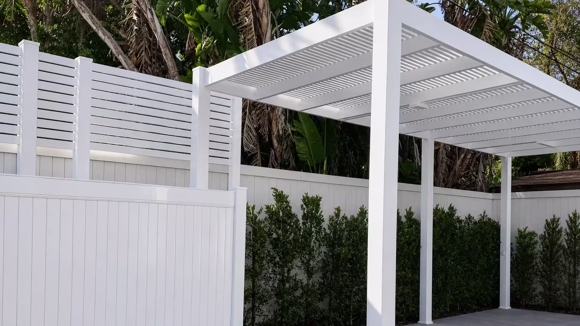Dense tropical foliage and a low side fence encircle this White vinyl picket patio cover