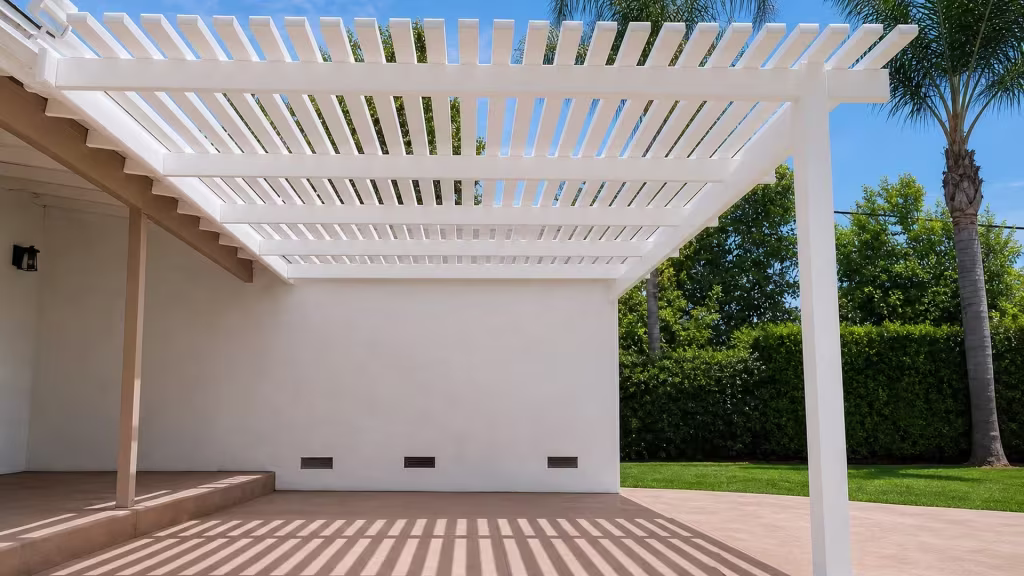 A stretch of lawn and mature palms fringe a White vinyl picket patio cover over a paved slab