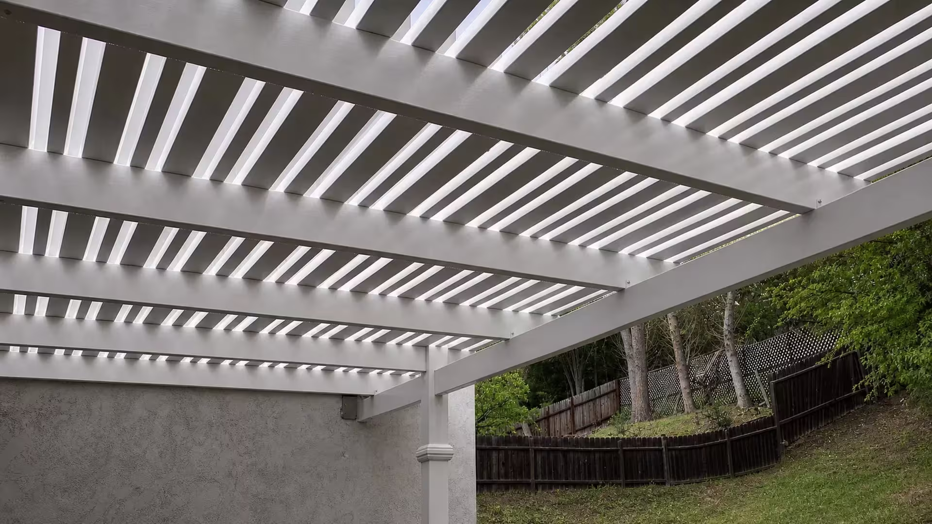 Graded, sloping ground and chain-link fencing run alongside a White vinyl picket patio cover