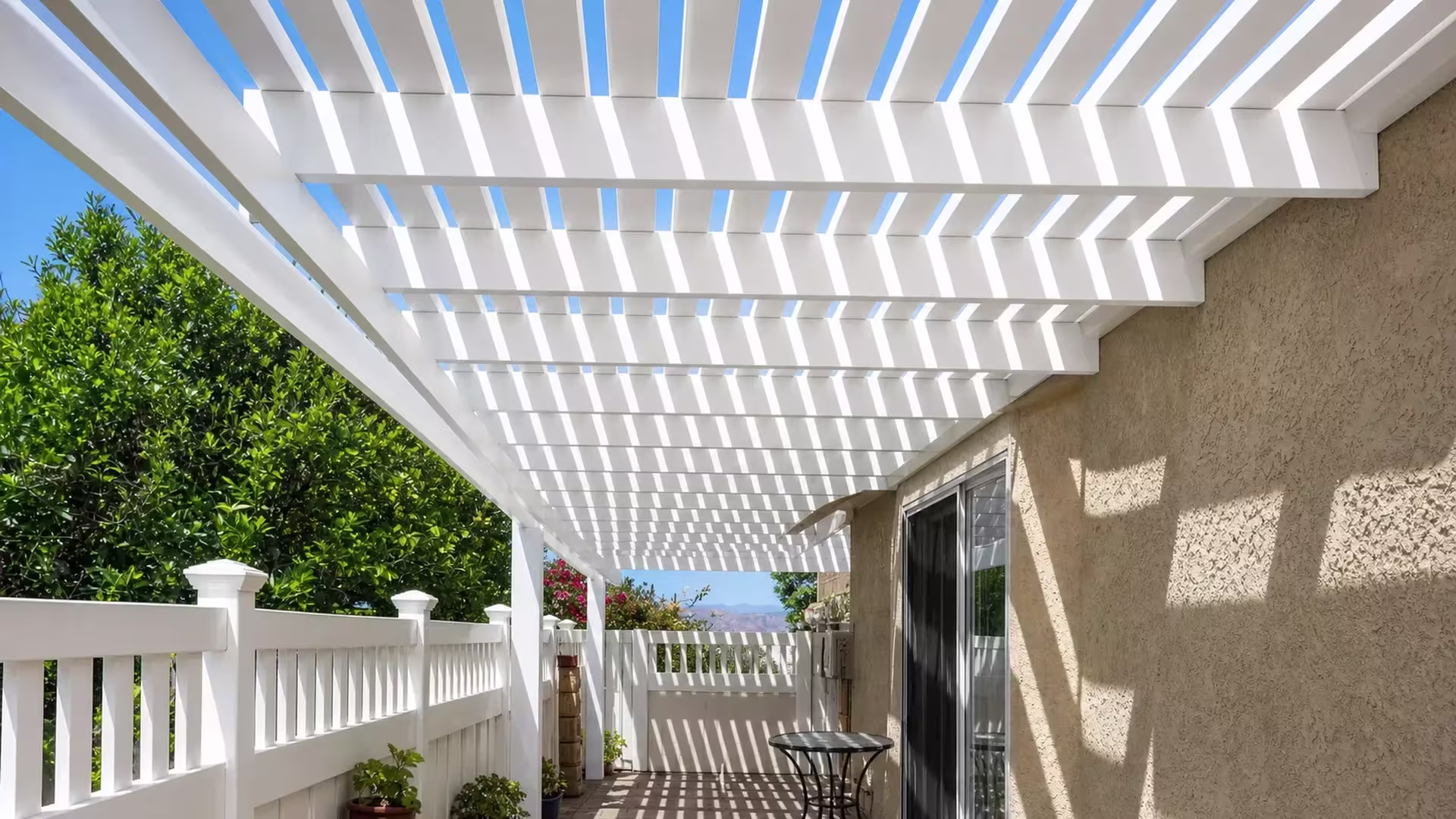 A sliding glass door and stucco overhang open onto this White vinyl picket patio cover