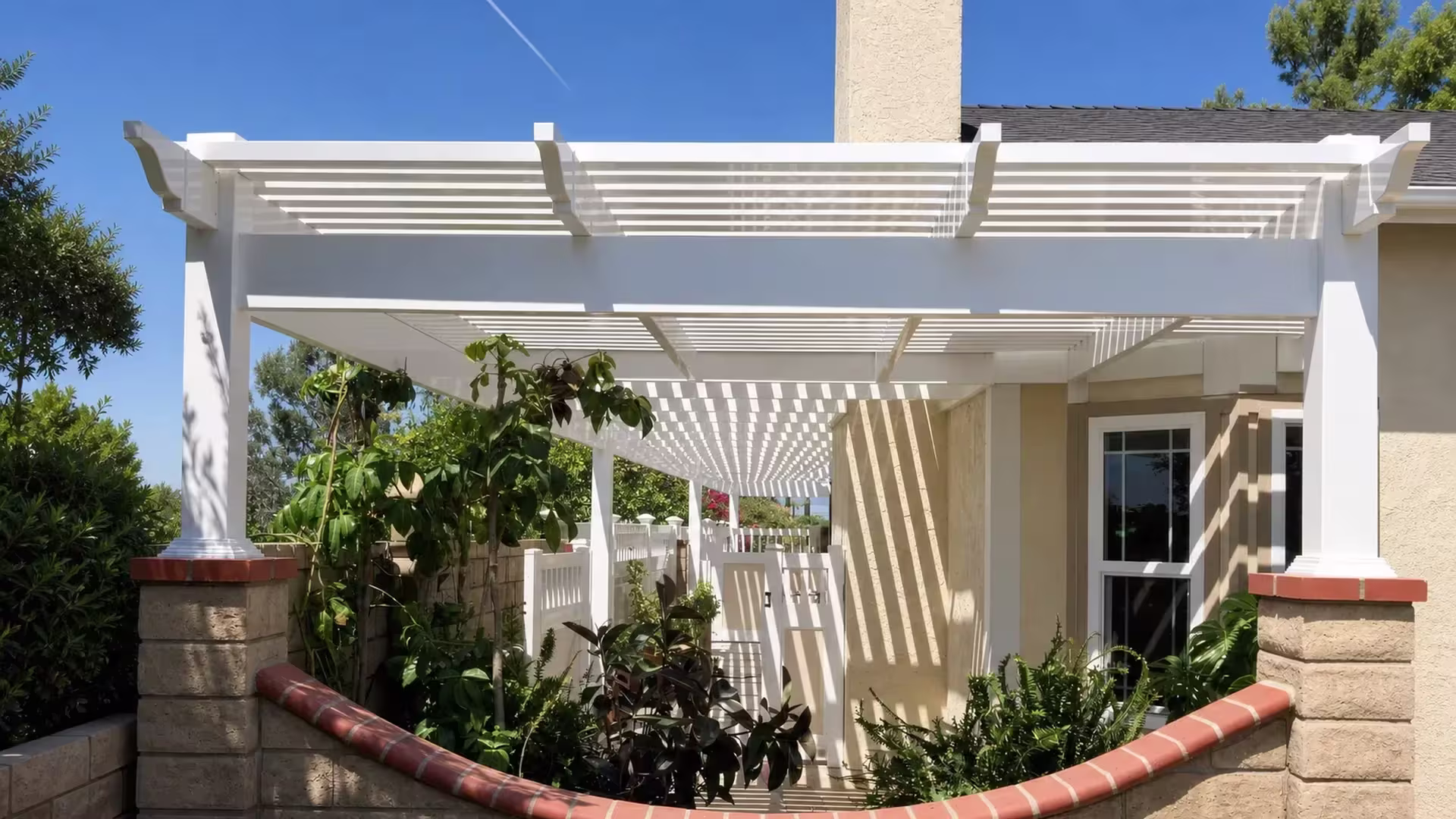 A red tile foreground wall and a chimney tower beside this White vinyl picket patio cover