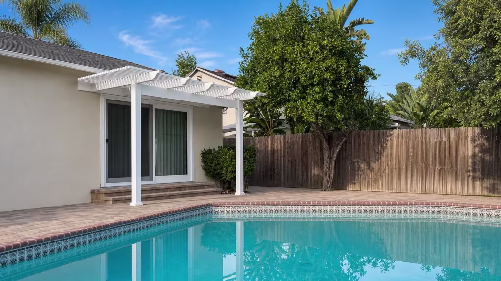 Decorative waterline pool tile and a fruit tree grow beside a White vinyl picket patio cover