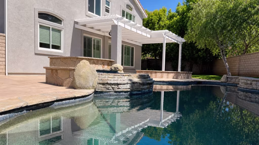 A raised stone spa with a spillway sits just below a White vinyl picket patio cover
