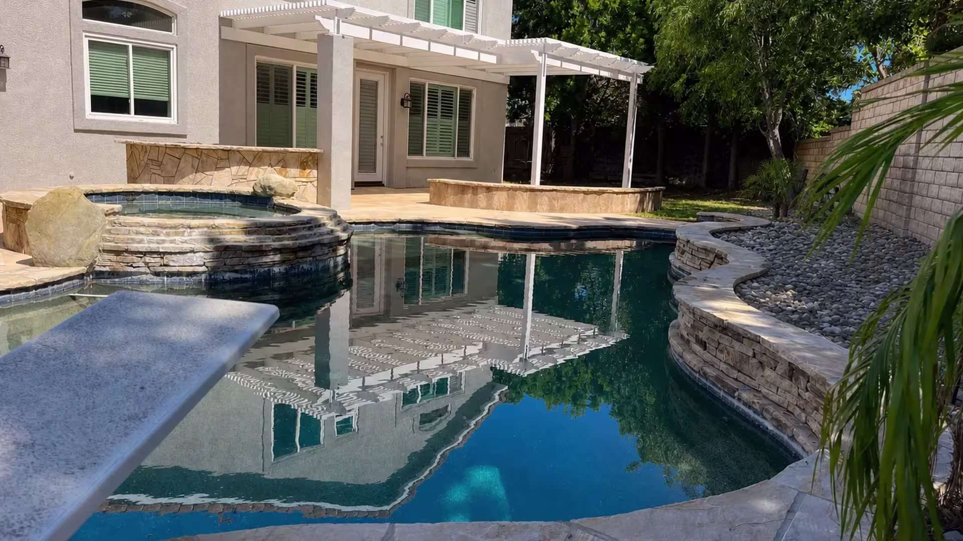 This White vinyl picket patio cover shelters a rear patio directly beside the swimming pool
