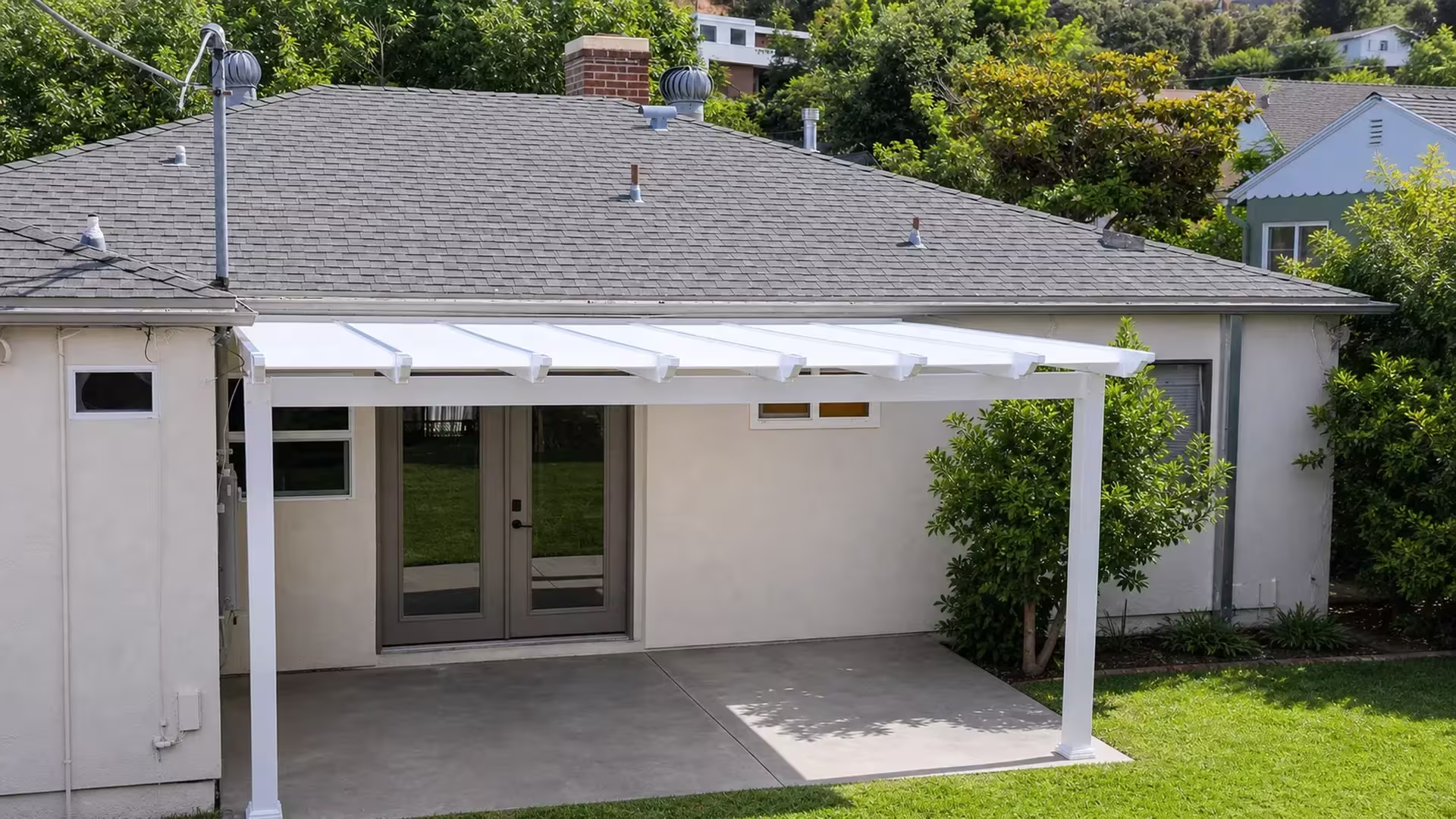 Gray stucco house with hillside homes beyond a White vinyl solid-roof picket patio cover