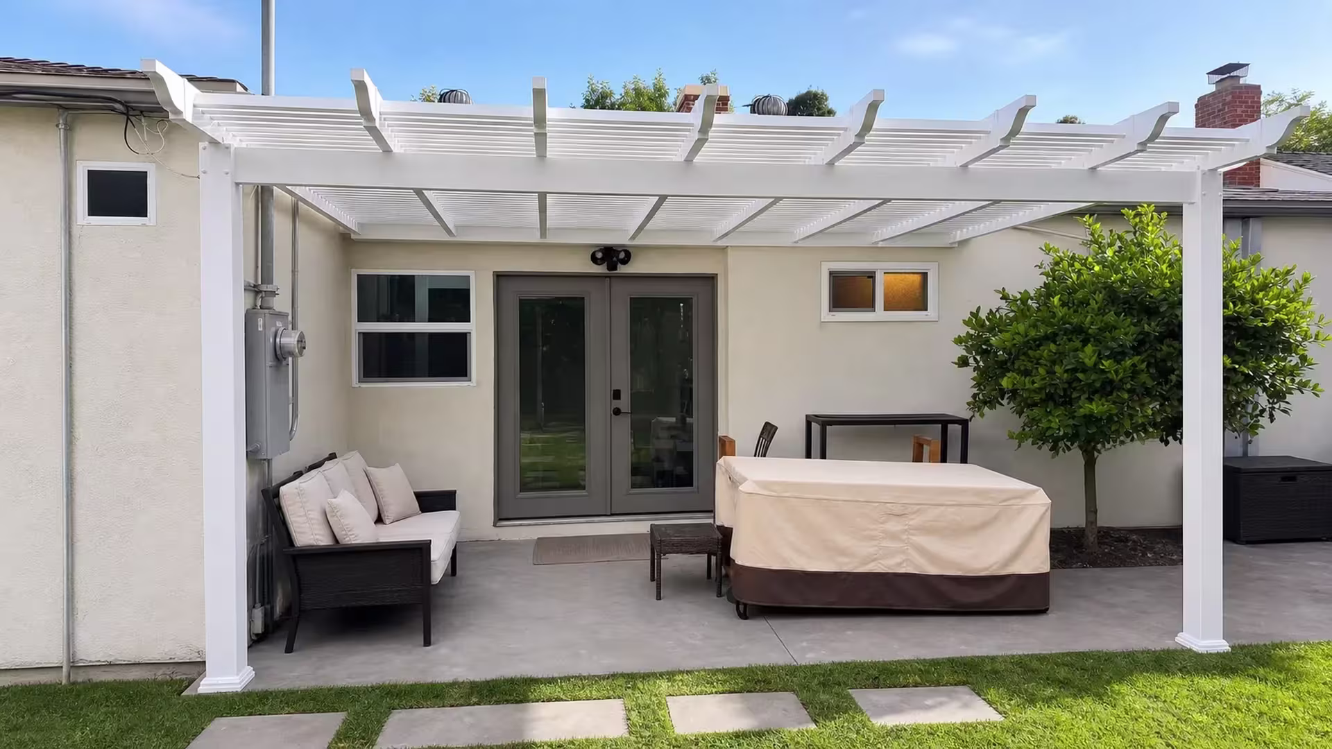 Cream stucco house bordered by a White vinyl lattice patio cover spanning the rear patio slab