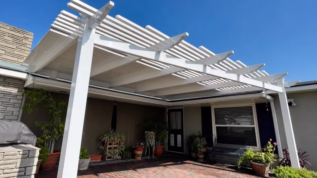 Brick paving and a masonry barbecue sit under a White vinyl picket patio cover