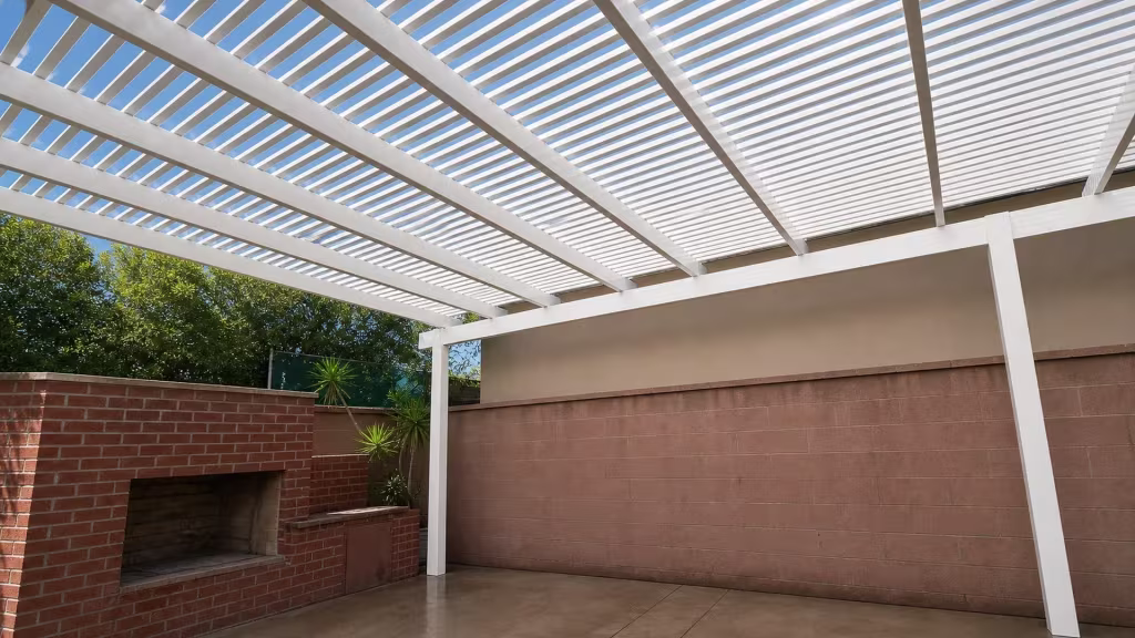 A red-brown concrete-block wall borders this White vinyl slatted picket patio cover with open roof construction