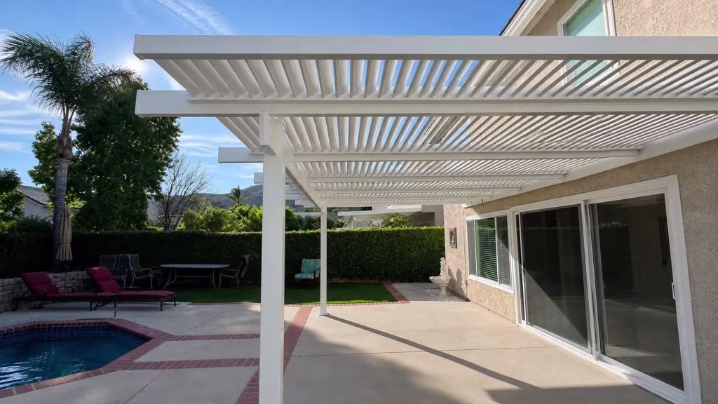 Sliding glass door and pool edge sit beneath a lattice-style White vinyl patio cover mounted along a stucco wall