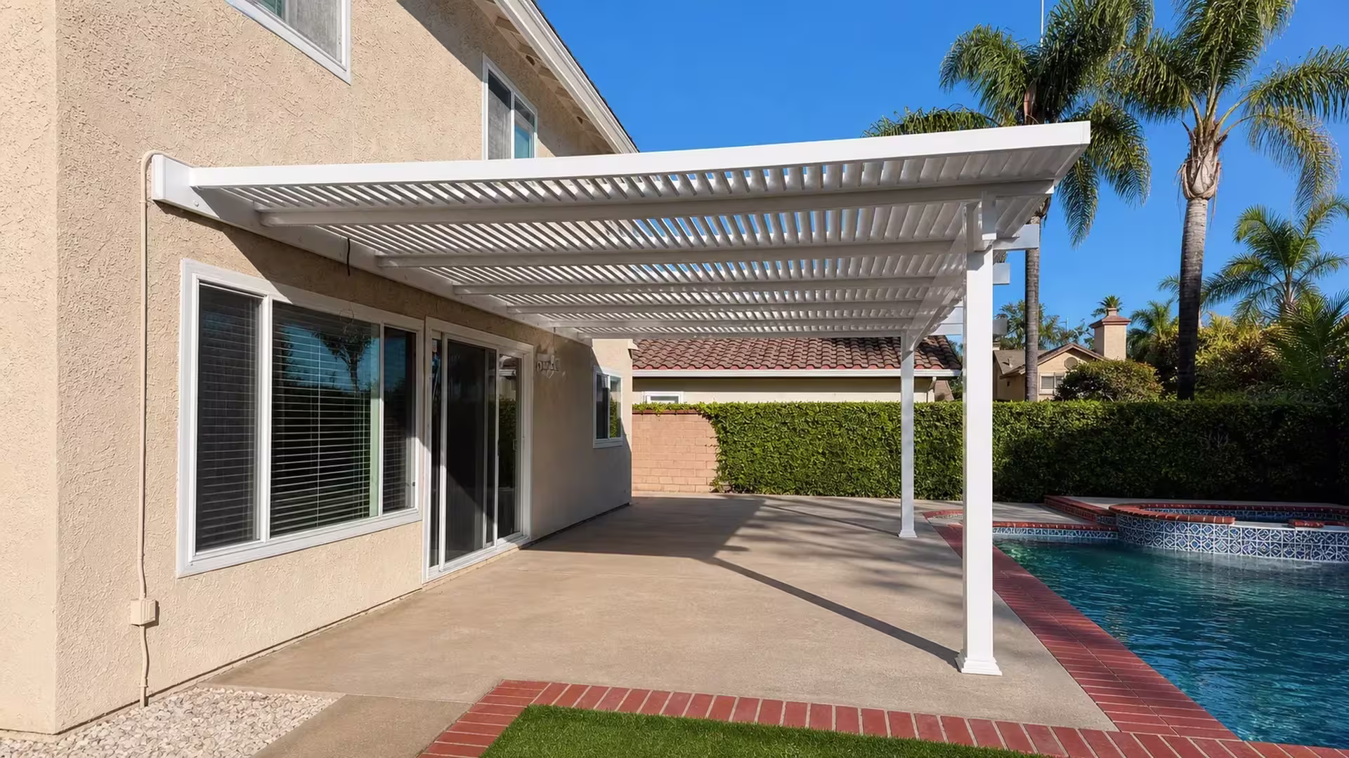 Beige stucco wall carries the ledger of this White vinyl house-attached lattice patio cover above the pool