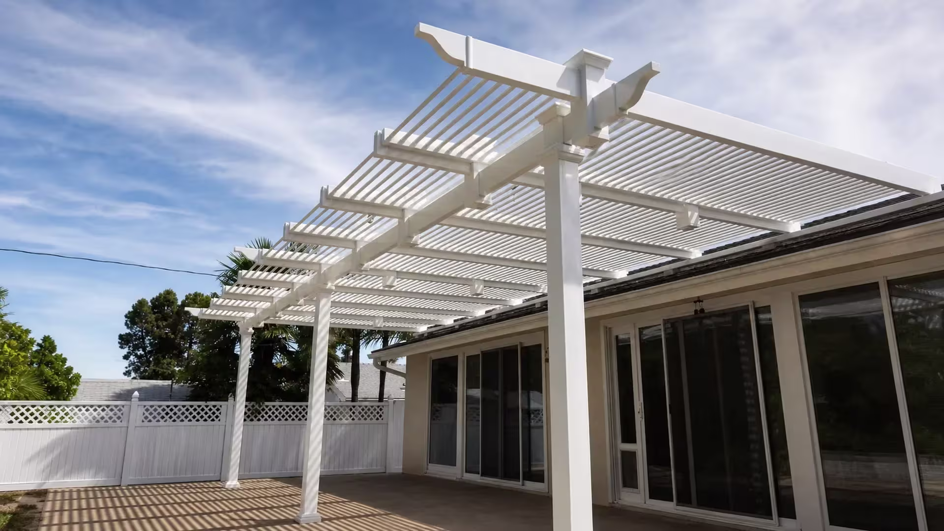 Rear lattice-topped fence stands near this White vinyl attached picket patio cover beside sliding glass doors
