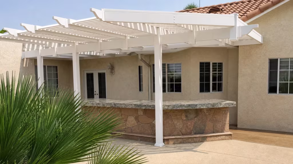 An outdoor bar counter stands beneath a White vinyl picket patio cover topped by a clay tile roofline