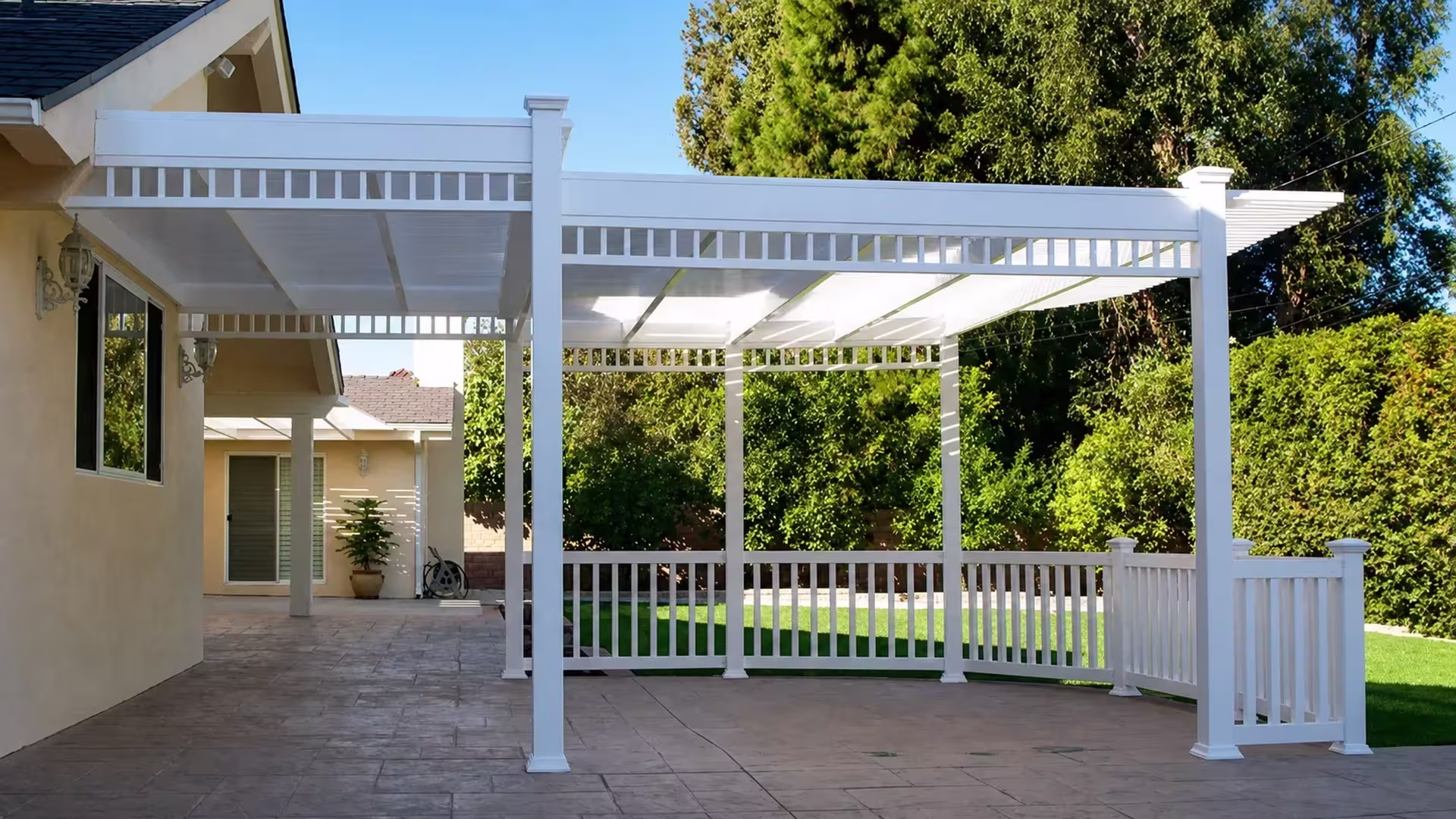 Two connected sections form this White vinyl solid-roof patio cover projecting across the patio from a beige house