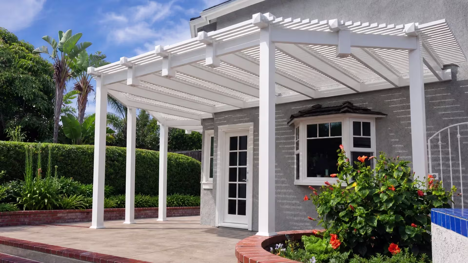 Stair rail and blue-tile patio edge run beneath a stepped, multi-bay White vinyl picket patio cover