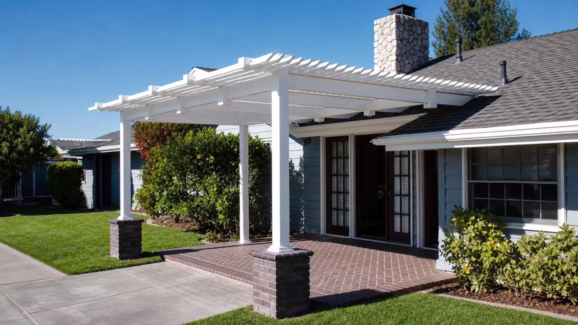 Dark brick masonry piers seat the front posts of a White vinyl patio cover below a stone chimney