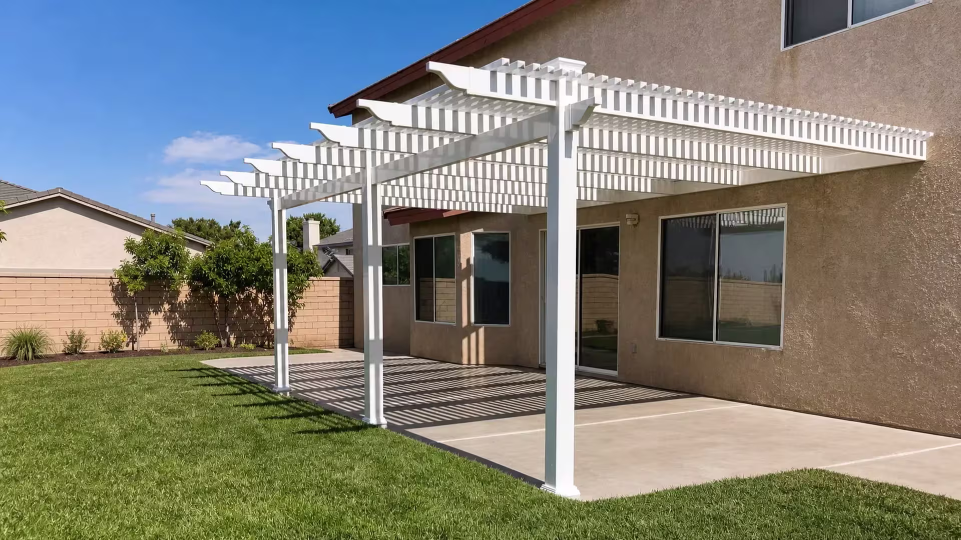White vinyl picket patio cover extending across a patio beside a two-story stucco house