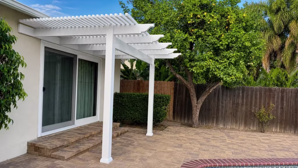 A mature citrus tree and weathered wood fence flank a White vinyl picket patio cover