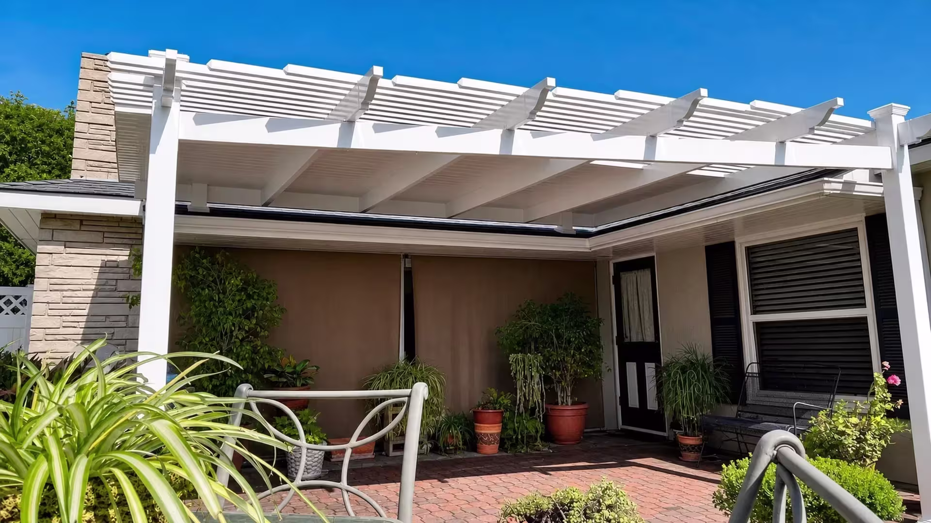L-shaped White vinyl picket patio cover wrapping a patio lined with stone masonry and metal furniture