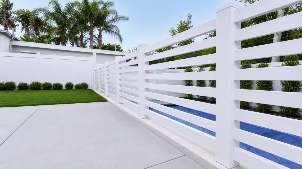 White vinyl horizontal picket pool fence angling past a blue covered pool surface toward tall capped posts