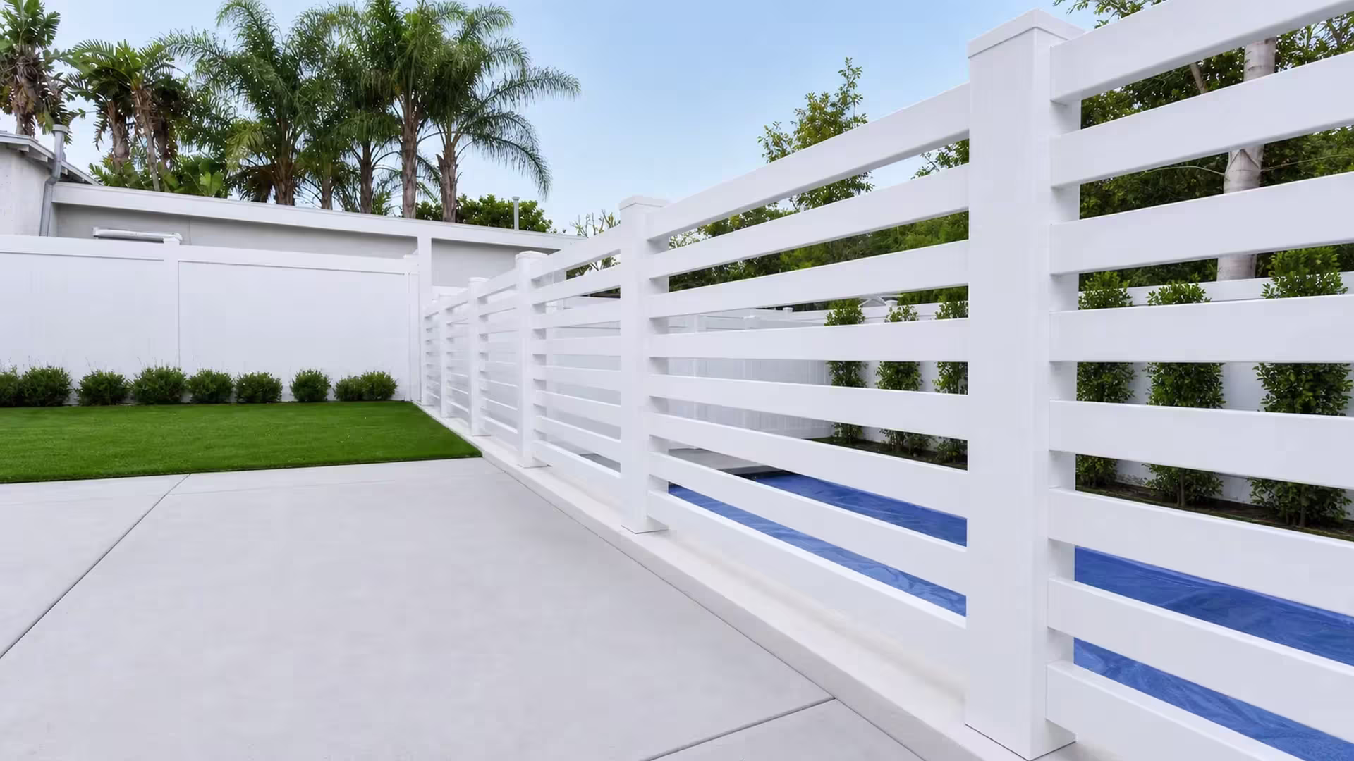 White vinyl horizontal picket pool fence angling past a blue covered pool surface toward tall capped posts