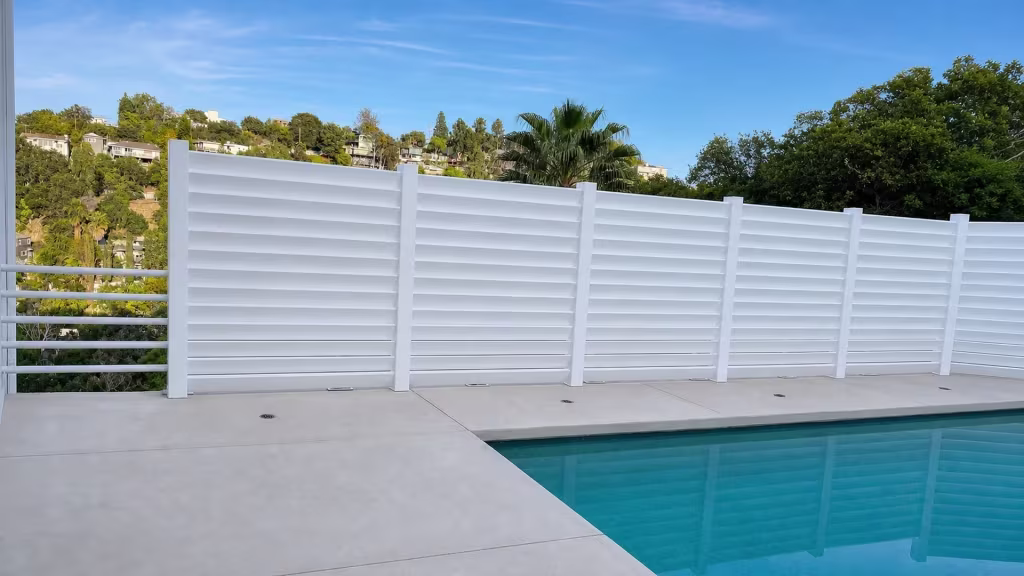 White vinyl horizontal louver pool fence in five connected bays following a graded hillside terrain beside the deck