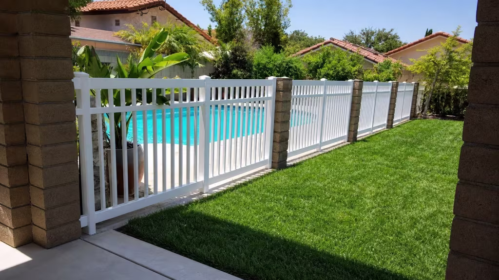 White vinyl pool fence with three horizontal rails set against neighboring stucco homes topped with clay-tile roofs