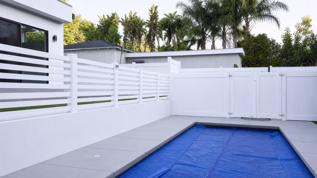 Stepped horizontal-slat bays of this White vinyl pool fence sit atop a raised block wall, turning at the rear corner