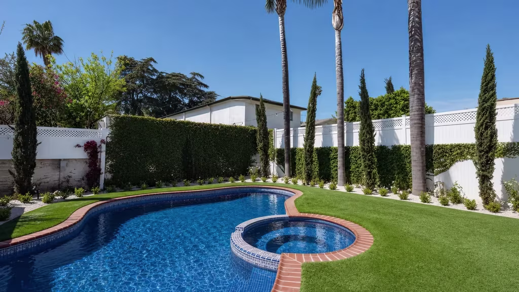 A lattice-topped section of White vinyl pool fence disappears behind a tall hedge beside a circular spa area