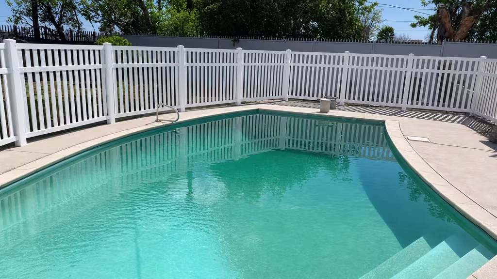 White vinyl pool fence with eight capped posts running the length of turquoise water beside a gray perimeter wall