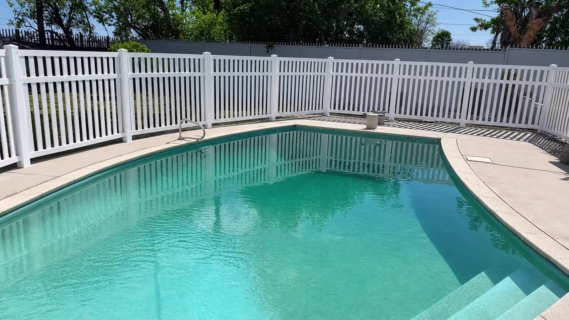 White vinyl pool fence with eight capped posts running the length of turquoise water beside a gray perimeter wall