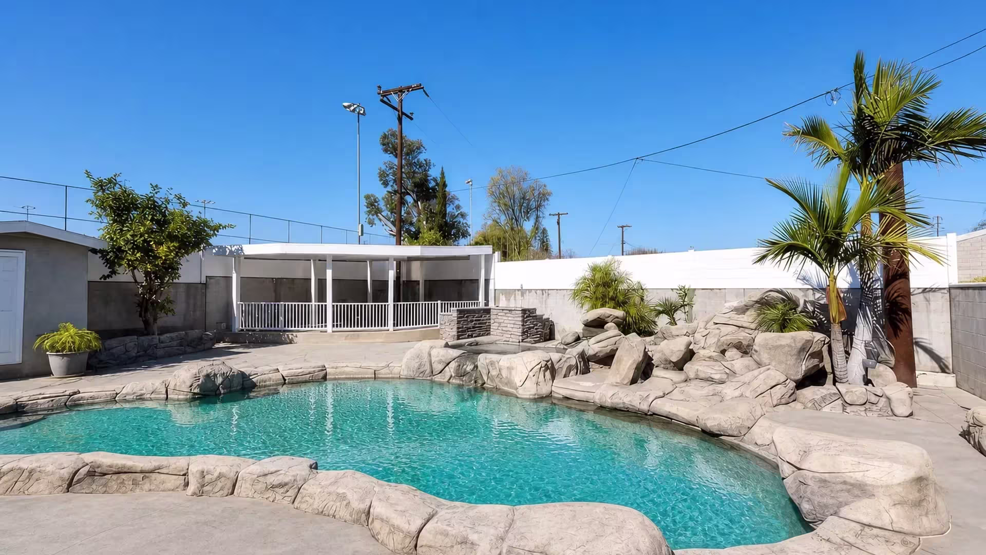 Along the edge of a raised rear patio, a White vinyl pool fence forms adjoining rectangular railing sections