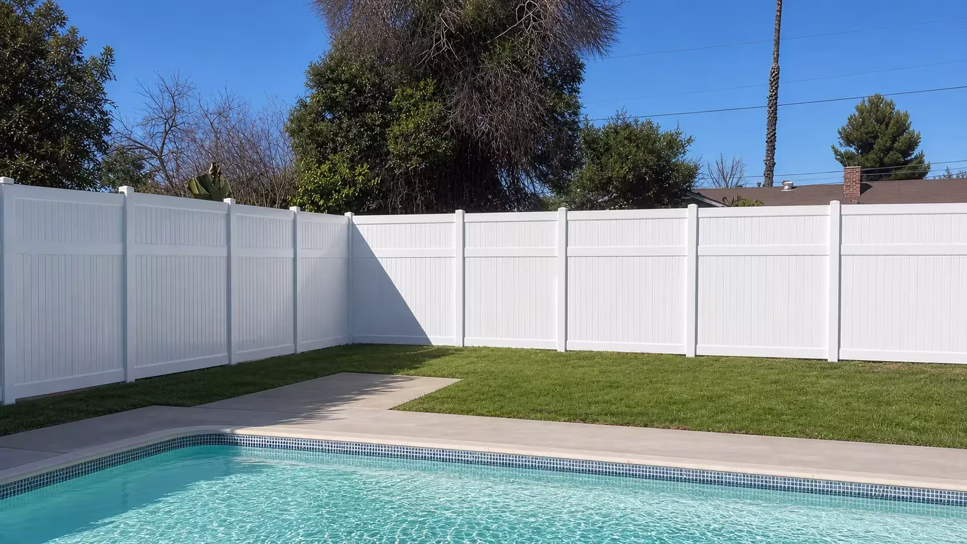 An L-shaped corner turn carries this White vinyl pool fence beneath a neighboring rooftop, boards fitted tongue-and-groove