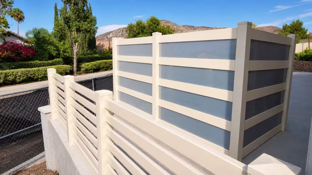 Mountain terrain rises behind this Tan vinyl privacy fence with acrylic set beside an old chain-link run