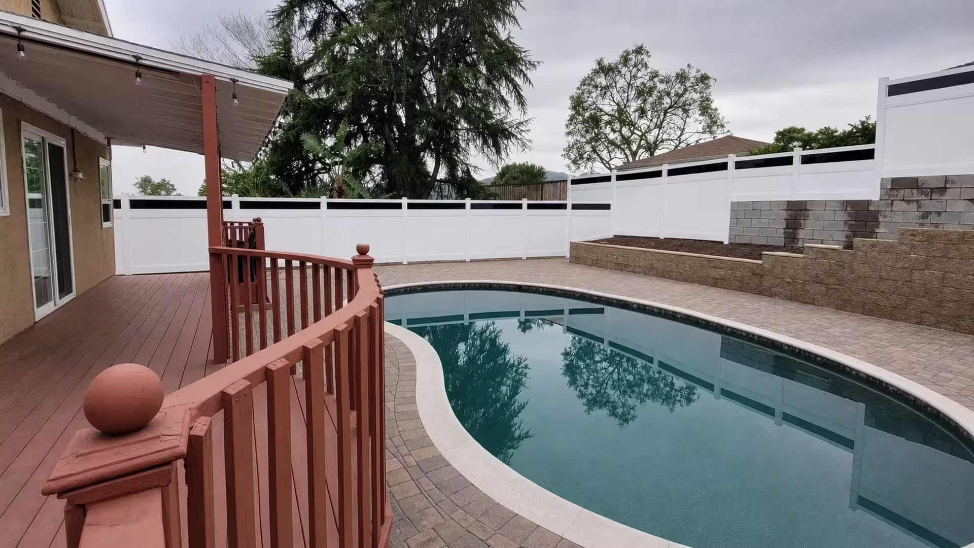 Terraced retaining wall steps up beneath this White vinyl privacy fence with acrylic beside a swimming pool