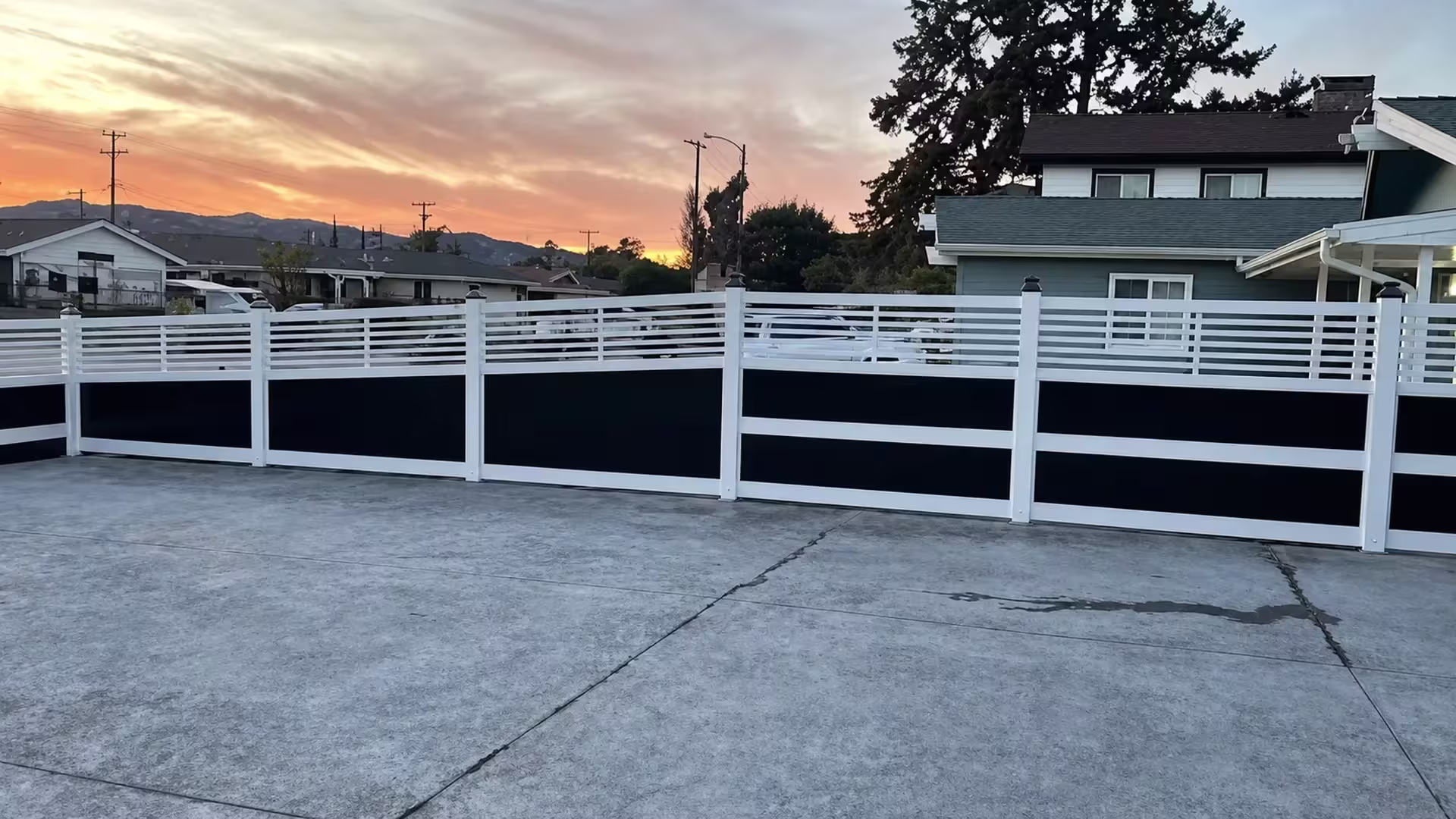 Cracked concrete pavement fronts this White vinyl privacy fence with dark charcoal acrylic panels