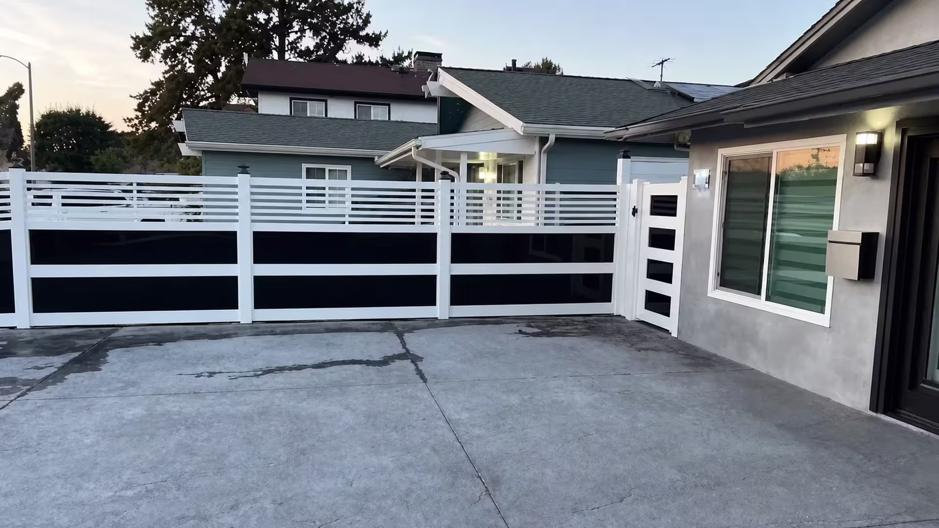 A black exterior door and patio cover sit beside this White vinyl privacy fence with acrylic framing a swinging gate